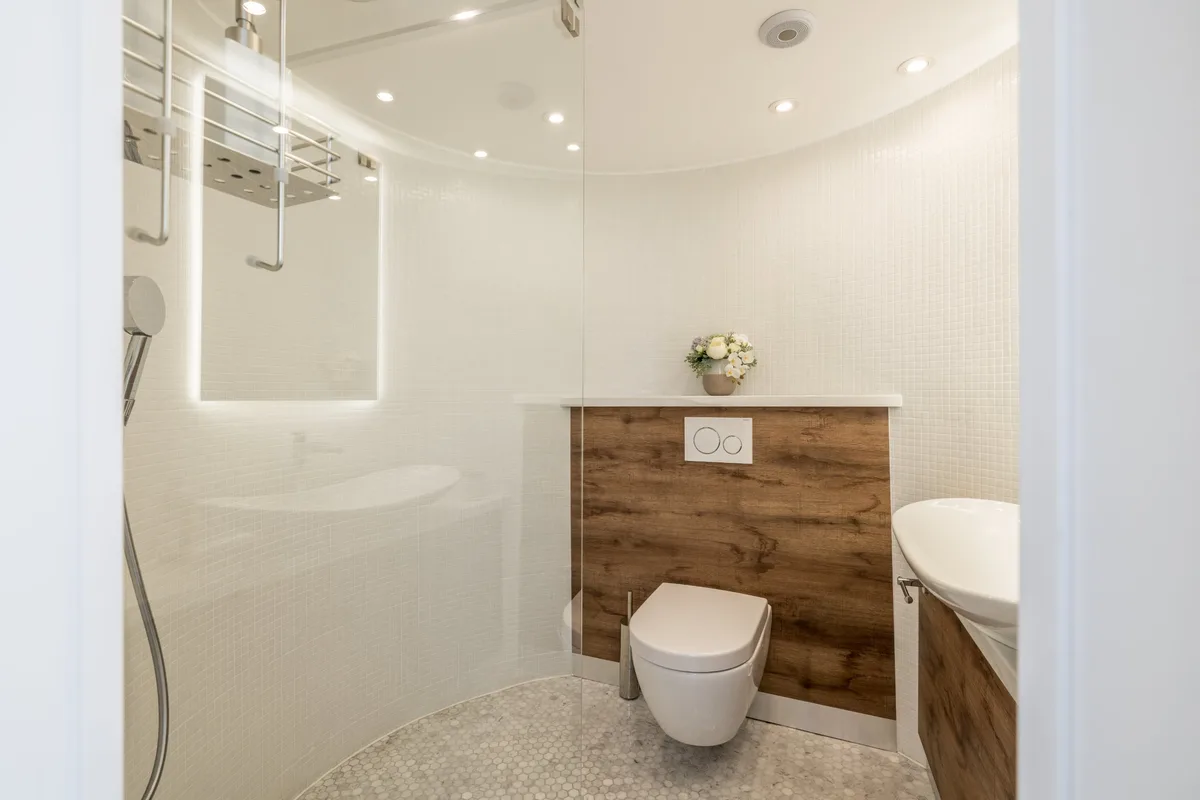 The round bathroom on the main deck: white mosaic walls, a glass shower screen, oak-panelled washstand