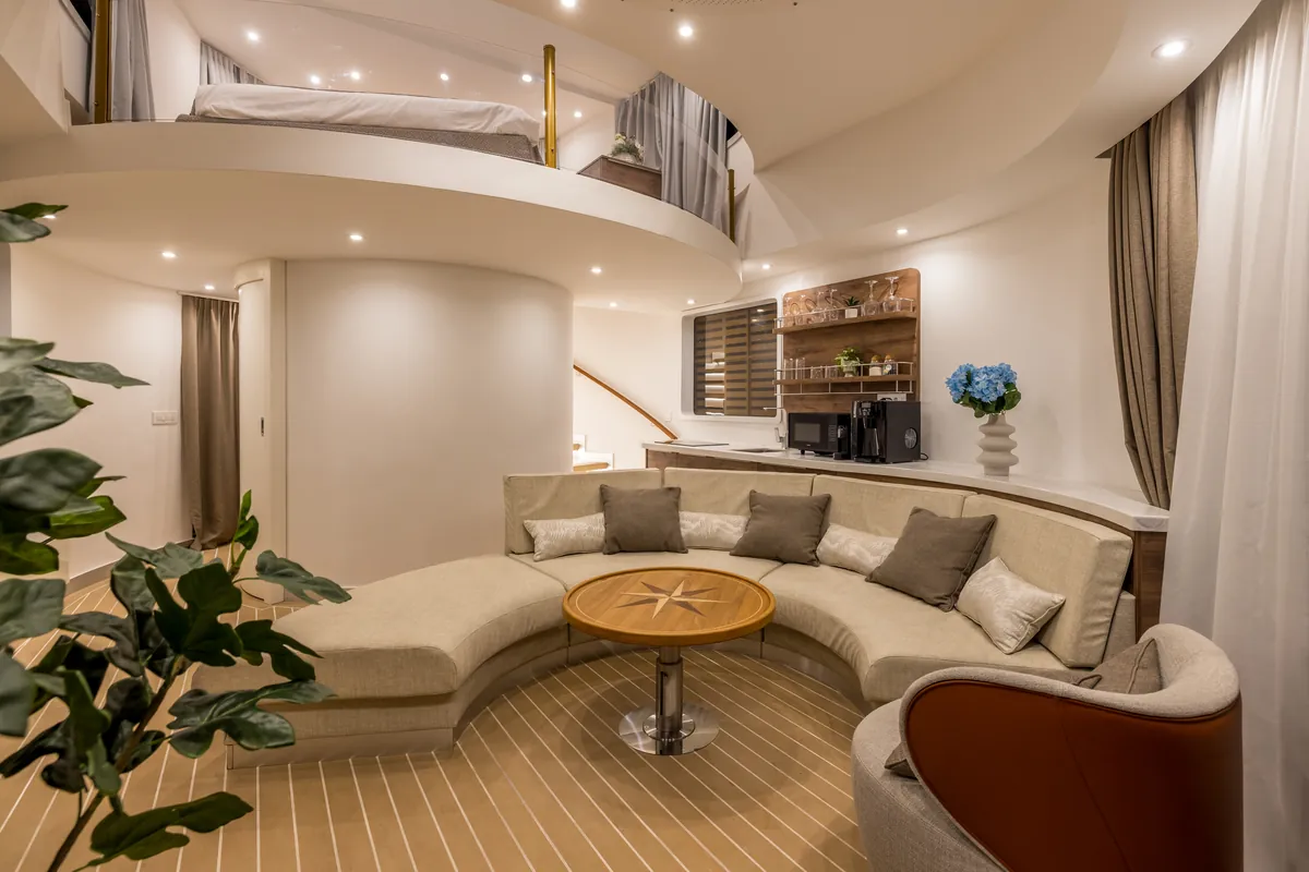 The living deck in the evening: a curved sofa and the kitchen, with the bedroom on the open upper deck above
